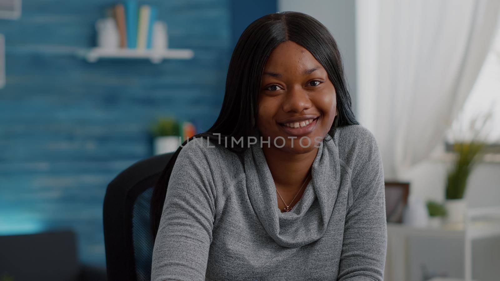 Portrait of student with black skin writing creative communication project for high school homework sitting at desk in living room. Teenager woman browsing graphic information on internet
