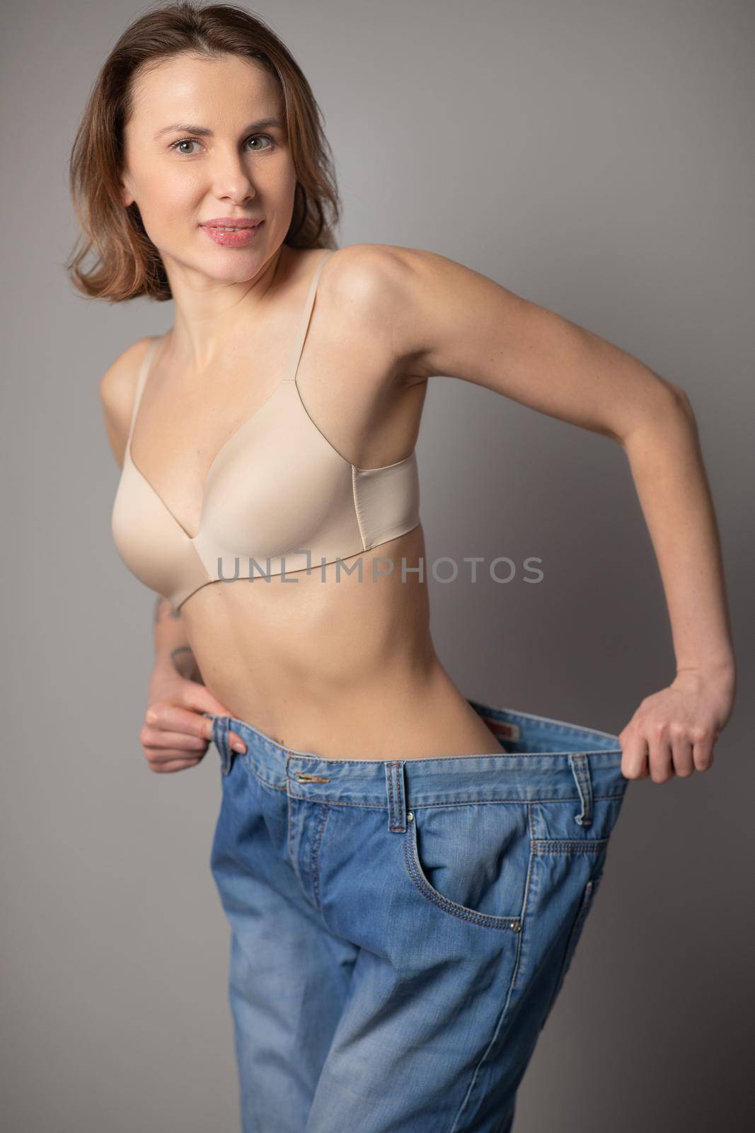 Woman Losing Weight After Diet, Slim Down, Burning Fat and Flat Waist. Thin Girl Show Weight Loss and Old Big Jeans. Skinny Female Belly Wearing Too Large Pants. by uflypro