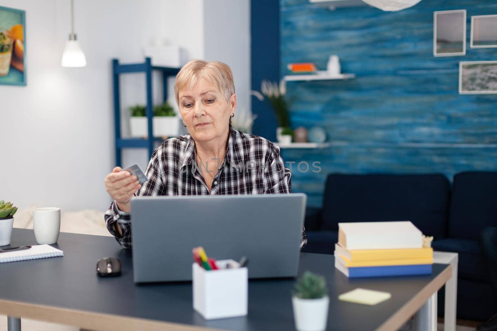 Senior woman learning to do bank operation using credit card. Joyful elderly woman using online banking for payment transcation surfing on internet from home living room.