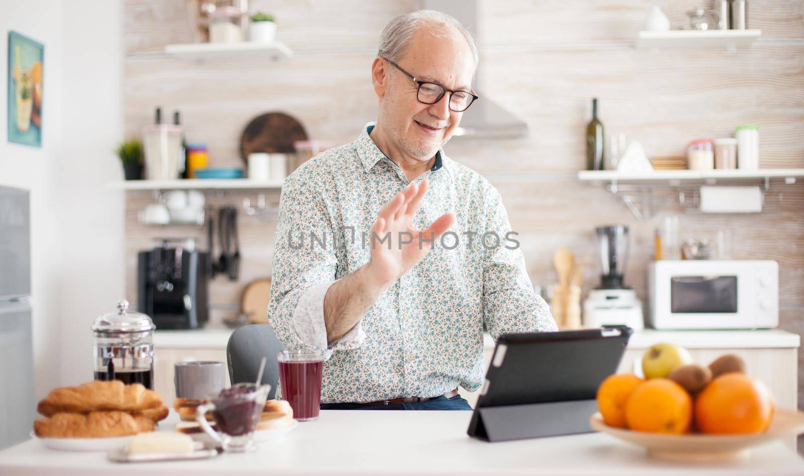 Authentic senior man on online video call in the morning in cozy kitchen. Elderly person using internet online chat technology video webcam making a video call connection camera communication conference call