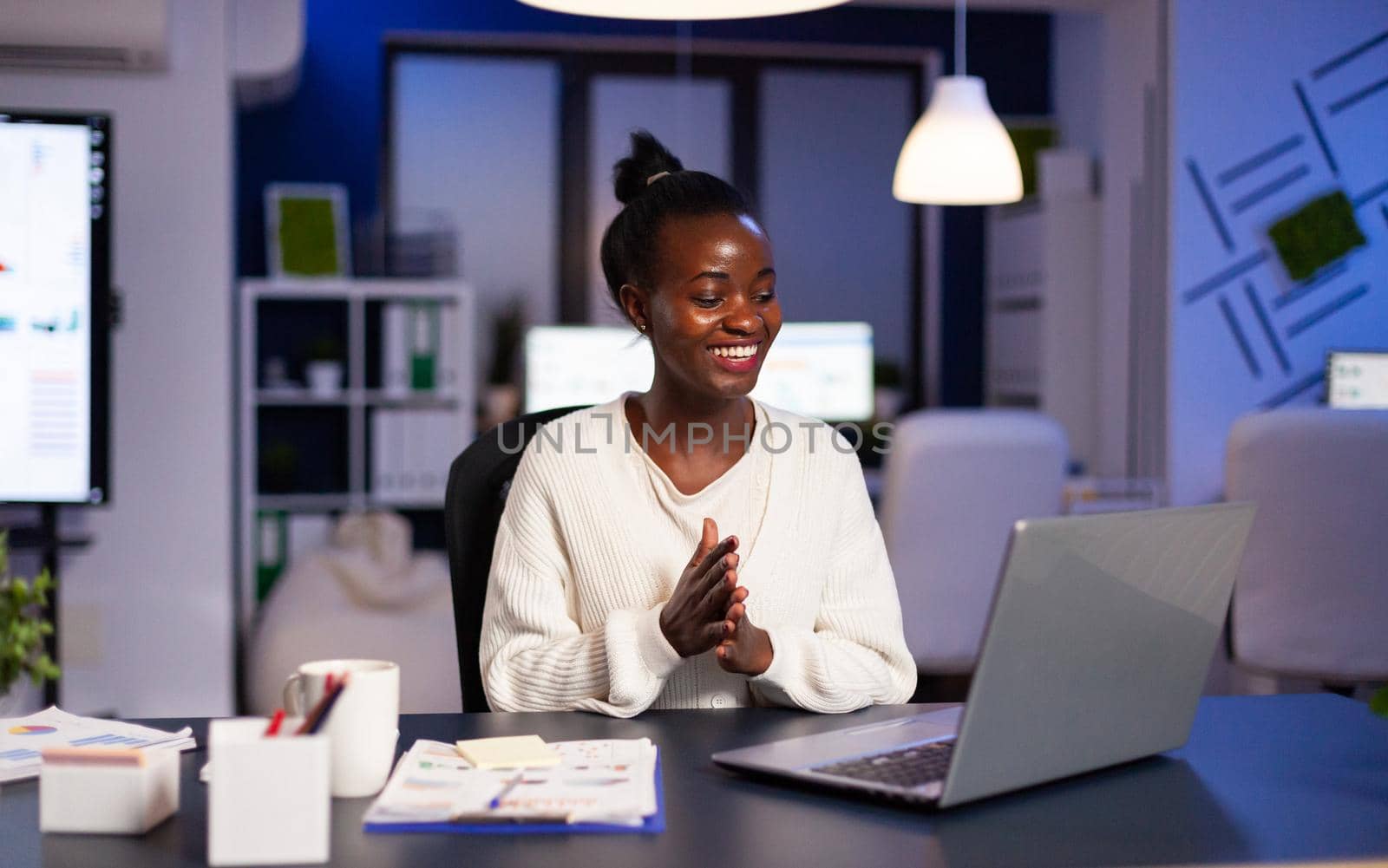 Happy african smiling because of positive results working lat at night in business office. Enthusiastic winner employee using modern technology celebrate online win success reading great data.