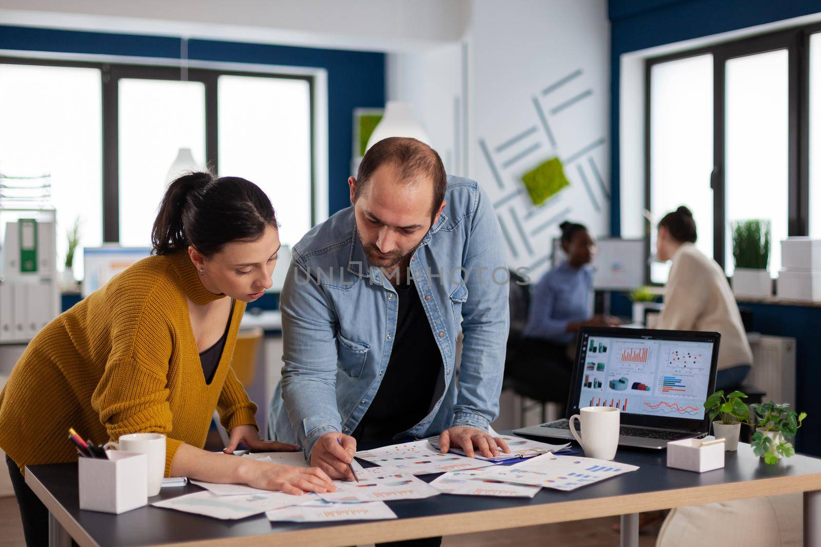 Multi ethnic coworkers team of start up consulting about marketing strategy. Diverse team of business people analyzing company financial reports from computer.