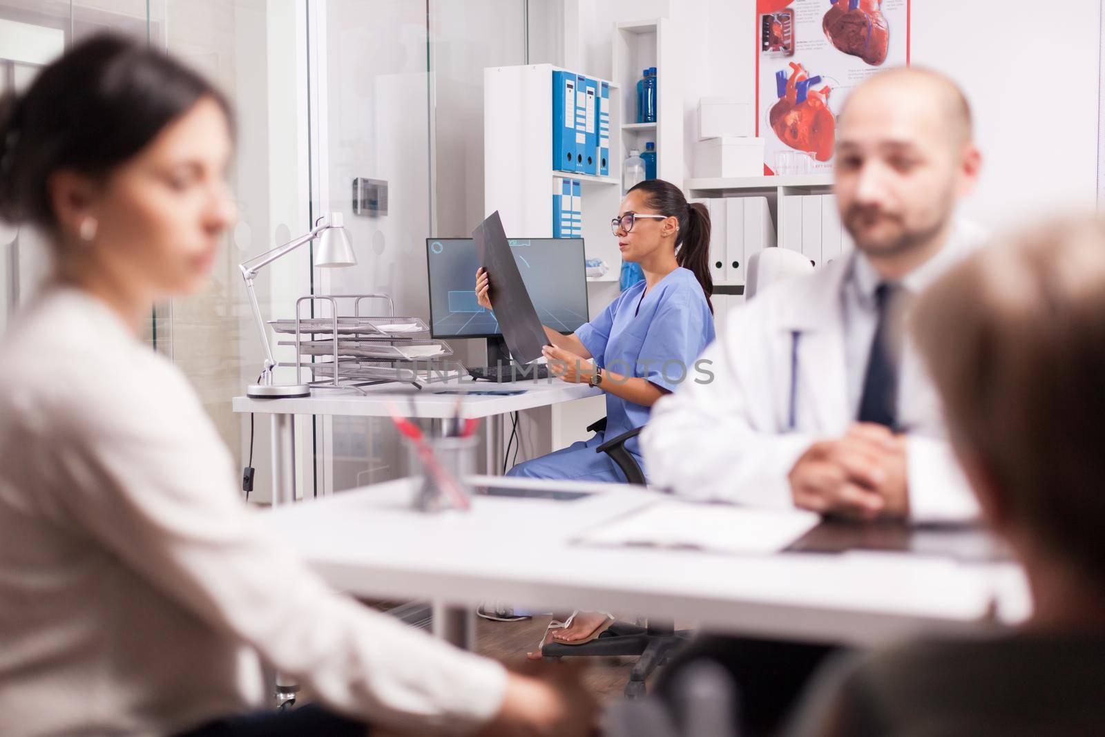 Nurse in blue uniform holding x-ray image in hospital office while doctor is consulting disabled senior woman in wheelchair. Young woman and her handicapped mother at medical check up.