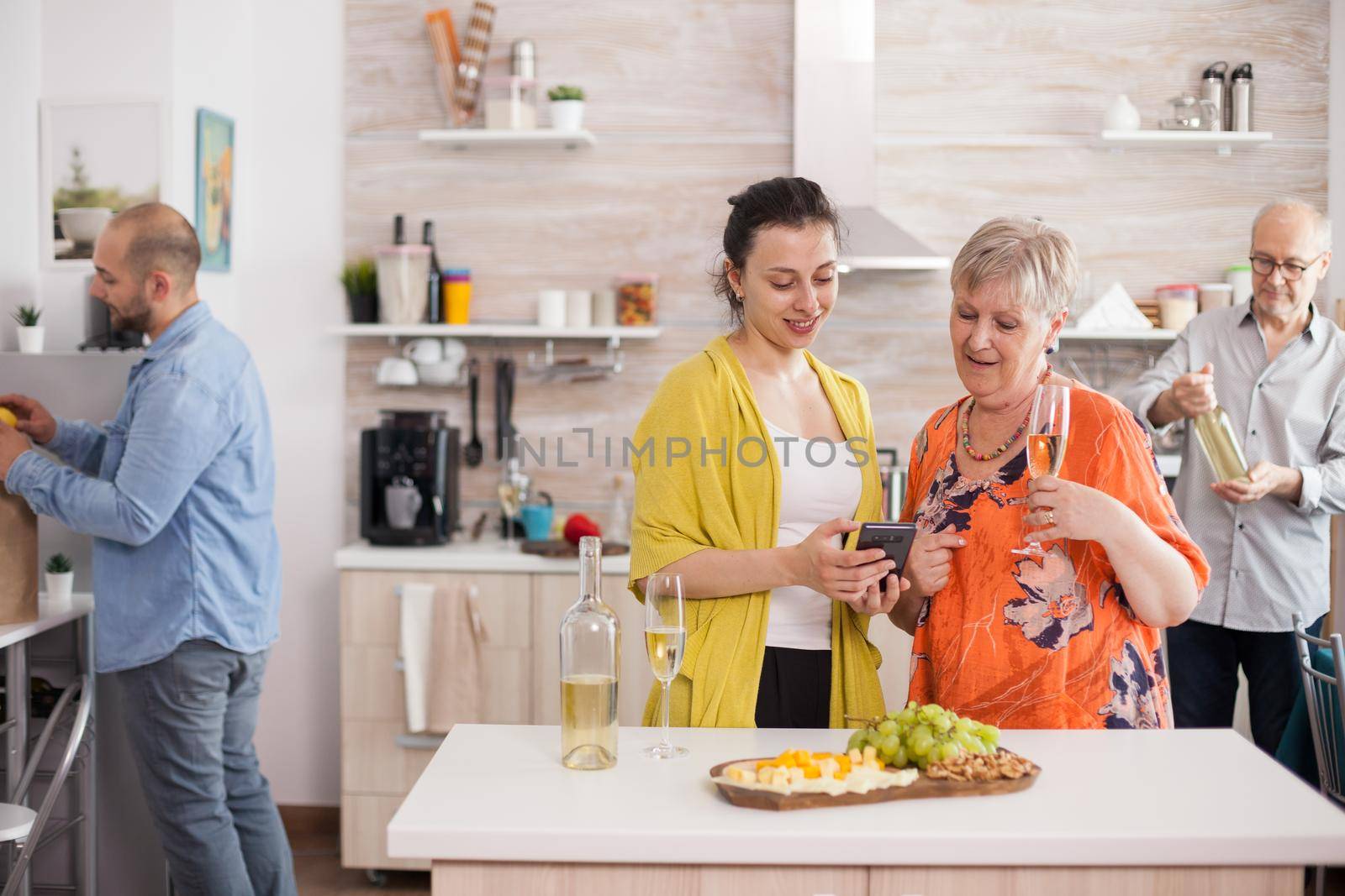 Mother and daughter smiling in kitchen using smarthphone drinking wine.