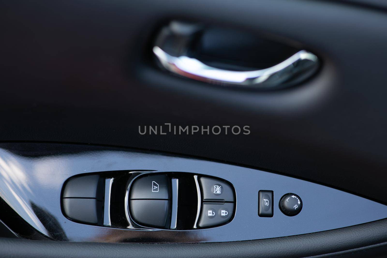 Detail on buttons controlling the windows in a car. Car interior details of door handle with windows controls and electric mirrors adjustments. Window and mirror control panel on driver's door by uflypro