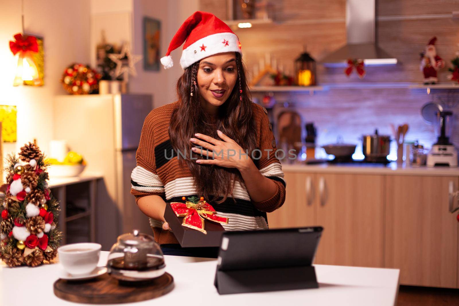 Happy woman using video call conference app on tablet giving virtual christmas present in festive home. Caucasian young person showing winter gifts with friends preparing for reunion