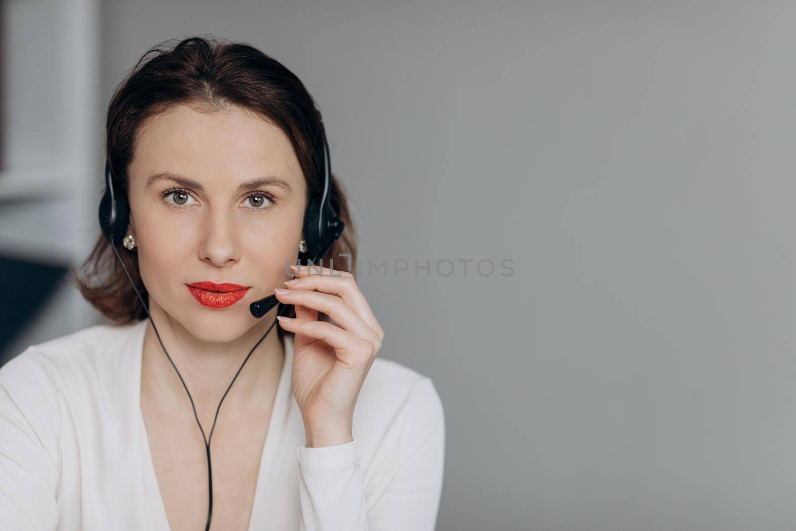 Pretty business woman talking with headset in a call center looking camera. Attractive young female customer service agent talking to a customer with a telephony headset as she looks at the camera.