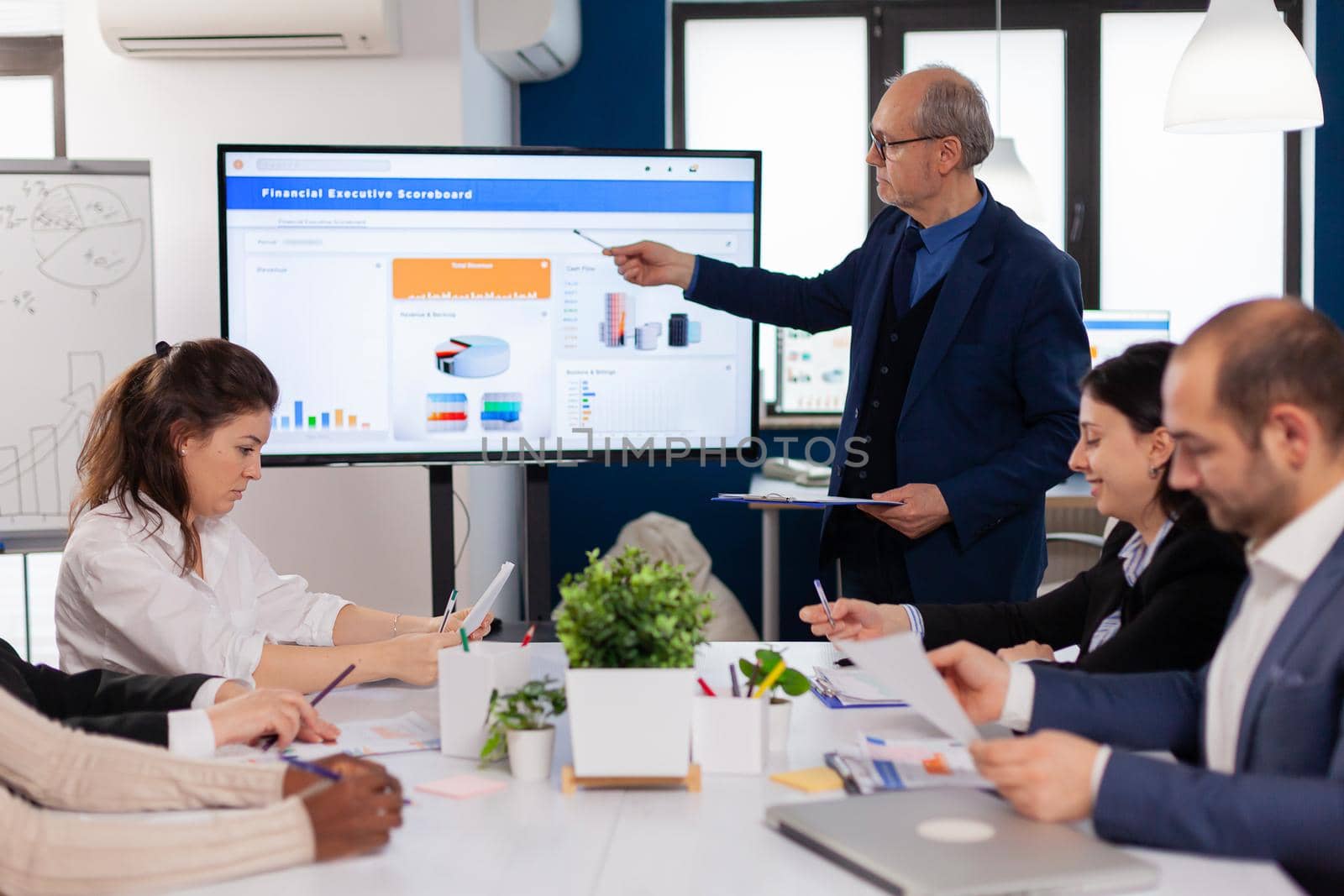 Senior team leader explaining presentation discussion in conference room briefing planning. Corporate staff discussing new business application with colleagues looking at screen