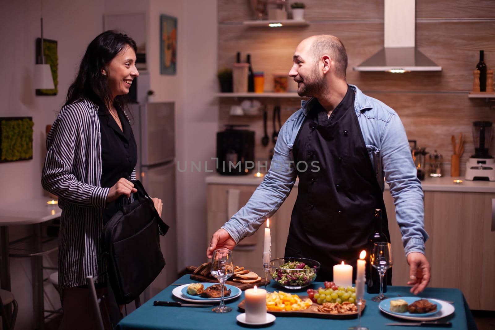 Wife smiling at husband in dining room while he's surprised with romantic dinner. Man preparing festive dinner with healthy food, cooking for his woman a romantic dinner,