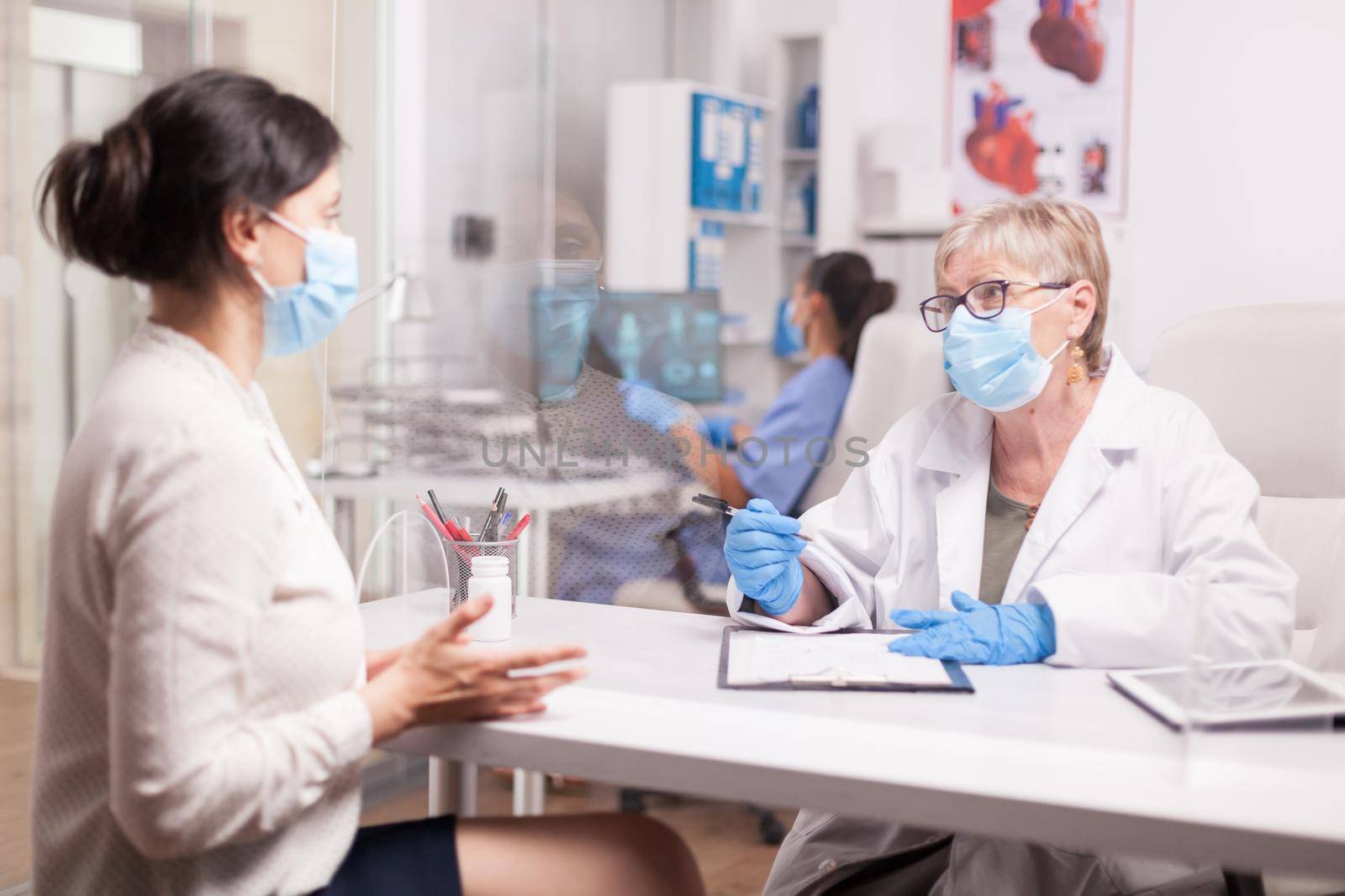 Mature doctor with face mask against coronavirus during consultation with sick young woman in hospital office.