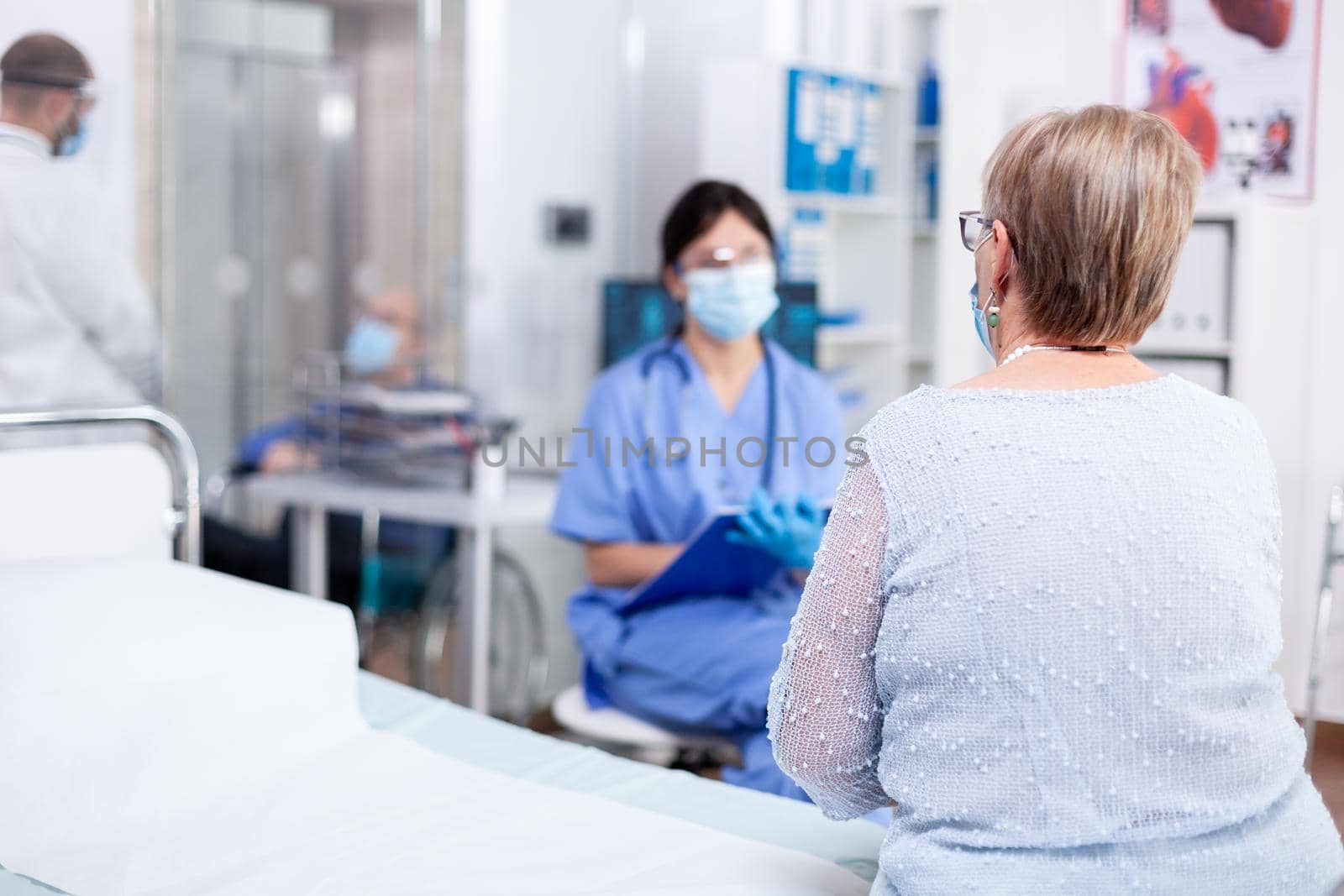 Senior woman wearing face mask against coronavirus outbreak listening nurse during consultation in hospital examination room. Modern private clinic or hospital. Practitioner physician appointment