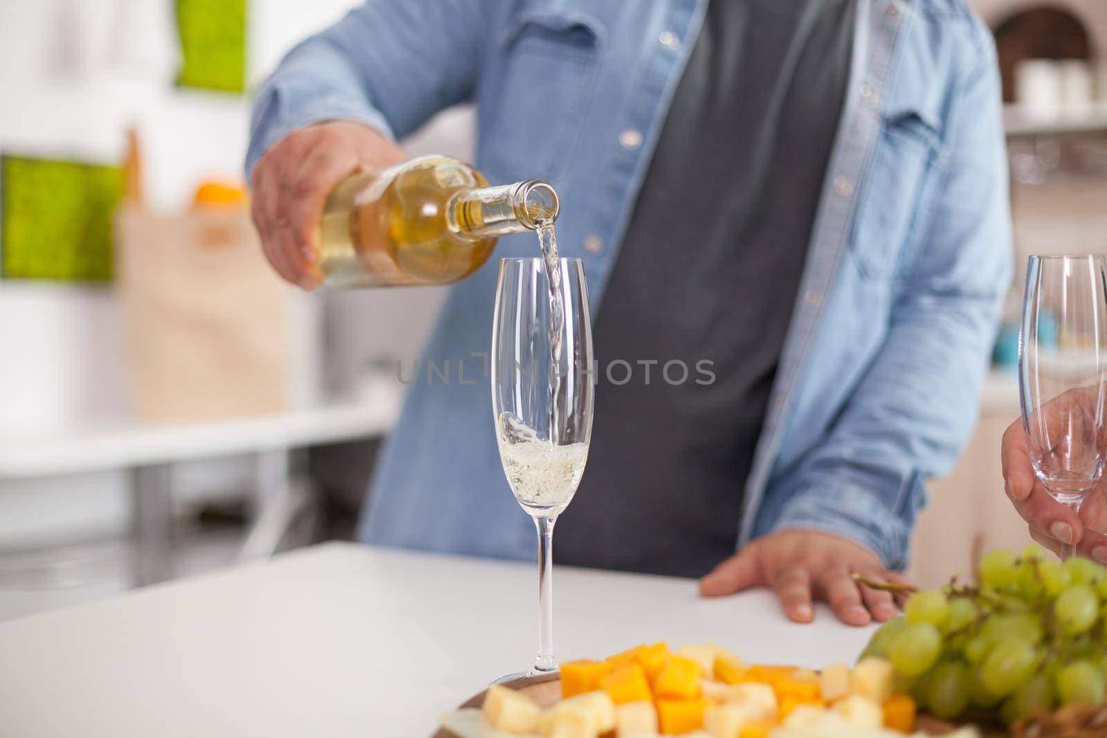 Close up of man pouring sparkling wine in glass on a table top in the kitchen.