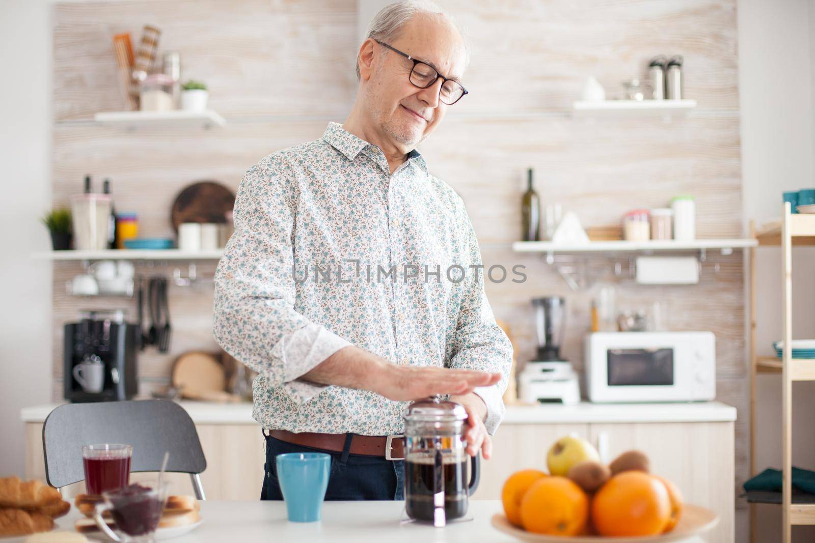 Elderly retired man using french press for coffee preparation in cozy bright kitchen. Senior person in the morning enjoying fresh brown cafe espresso cup caffeine from vintage mug, filter relax refreshment