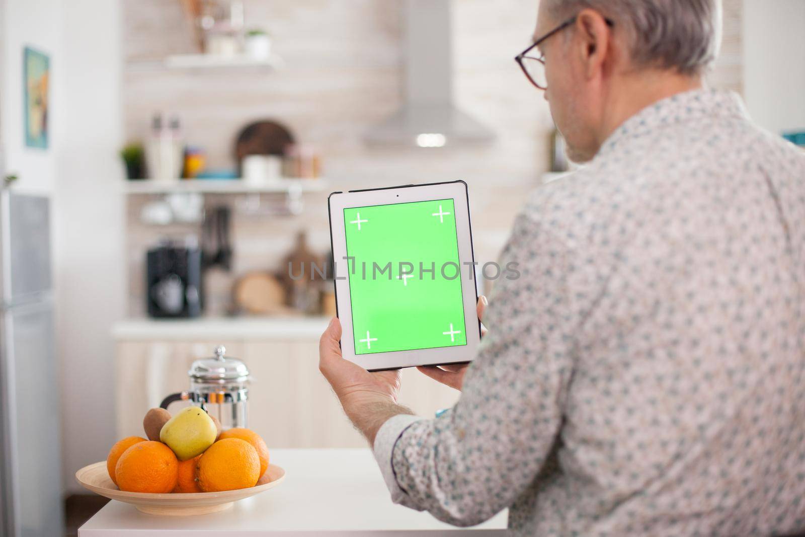 Grandfather looking at tablet pc with green screen during breakfast in kitchen. Elderly person with chroma key isolated mock-up mockup for easy replacement