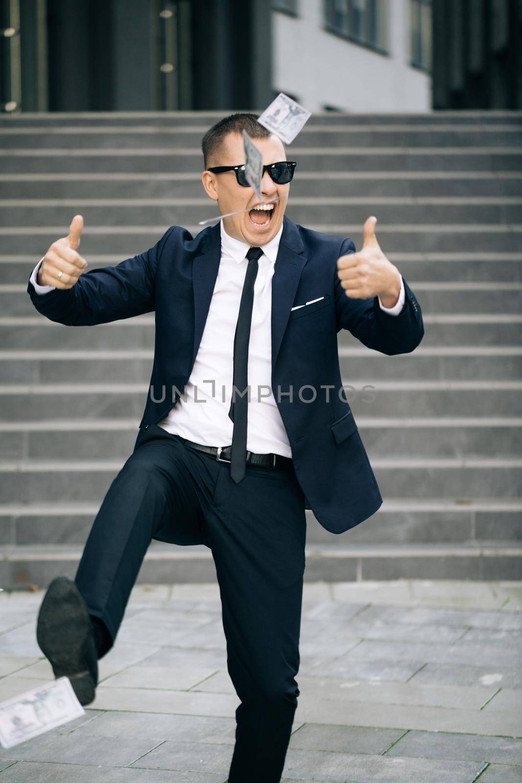 Money rain, falling dollars. Portrait shot of cheerful rich handsome businessman in glasses and suit throws money. Happy good looking man throwing dollars by uflypro