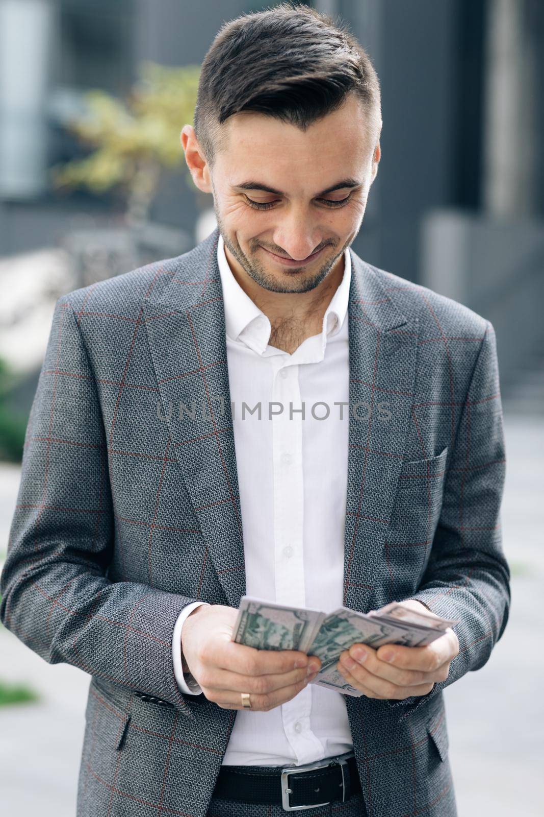 Handsome Rich Man Wearing Stylish Suit Counting Money Standing in the Street Near Office Building.