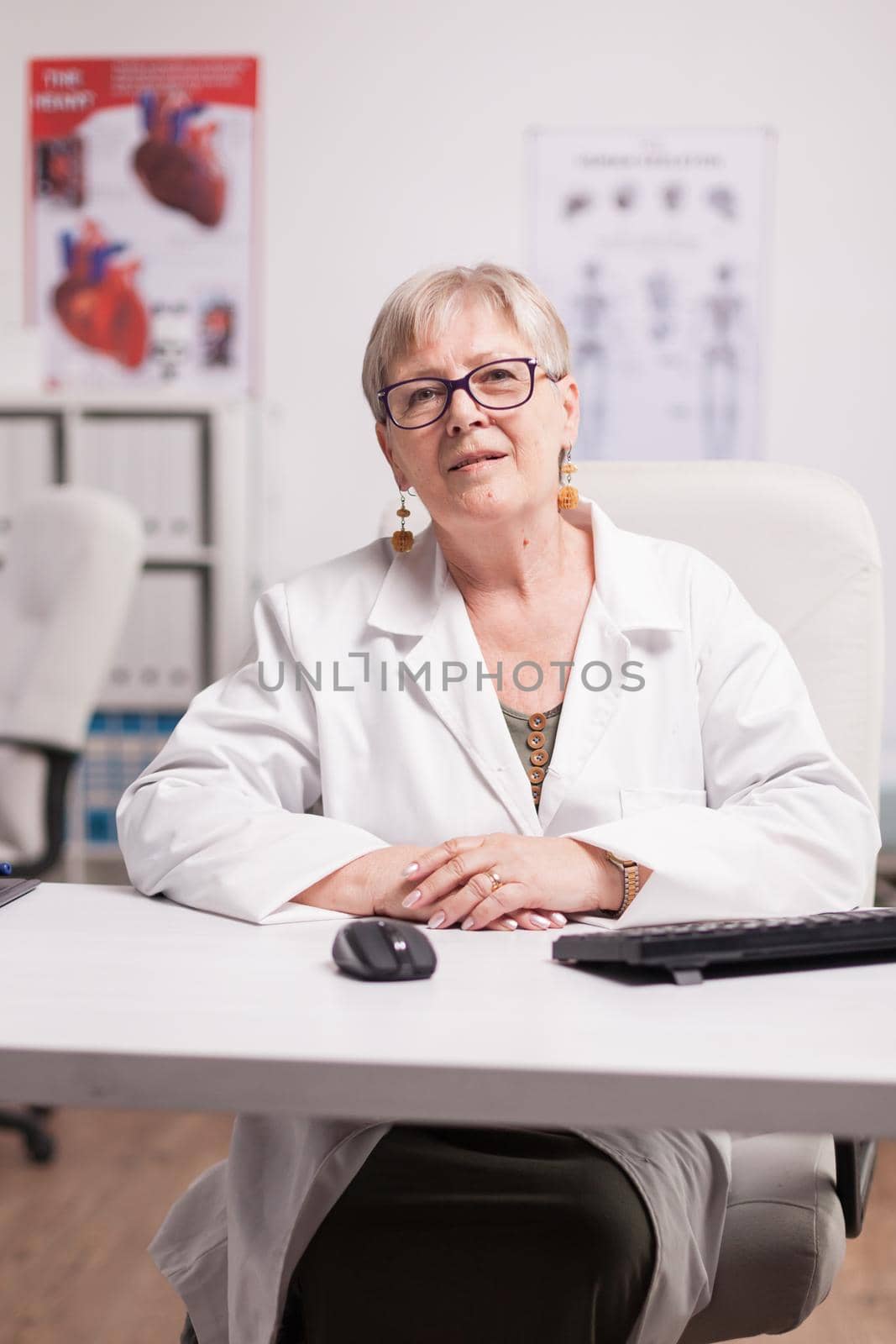 Mature female doctor in clinic cabinet looking at camera.