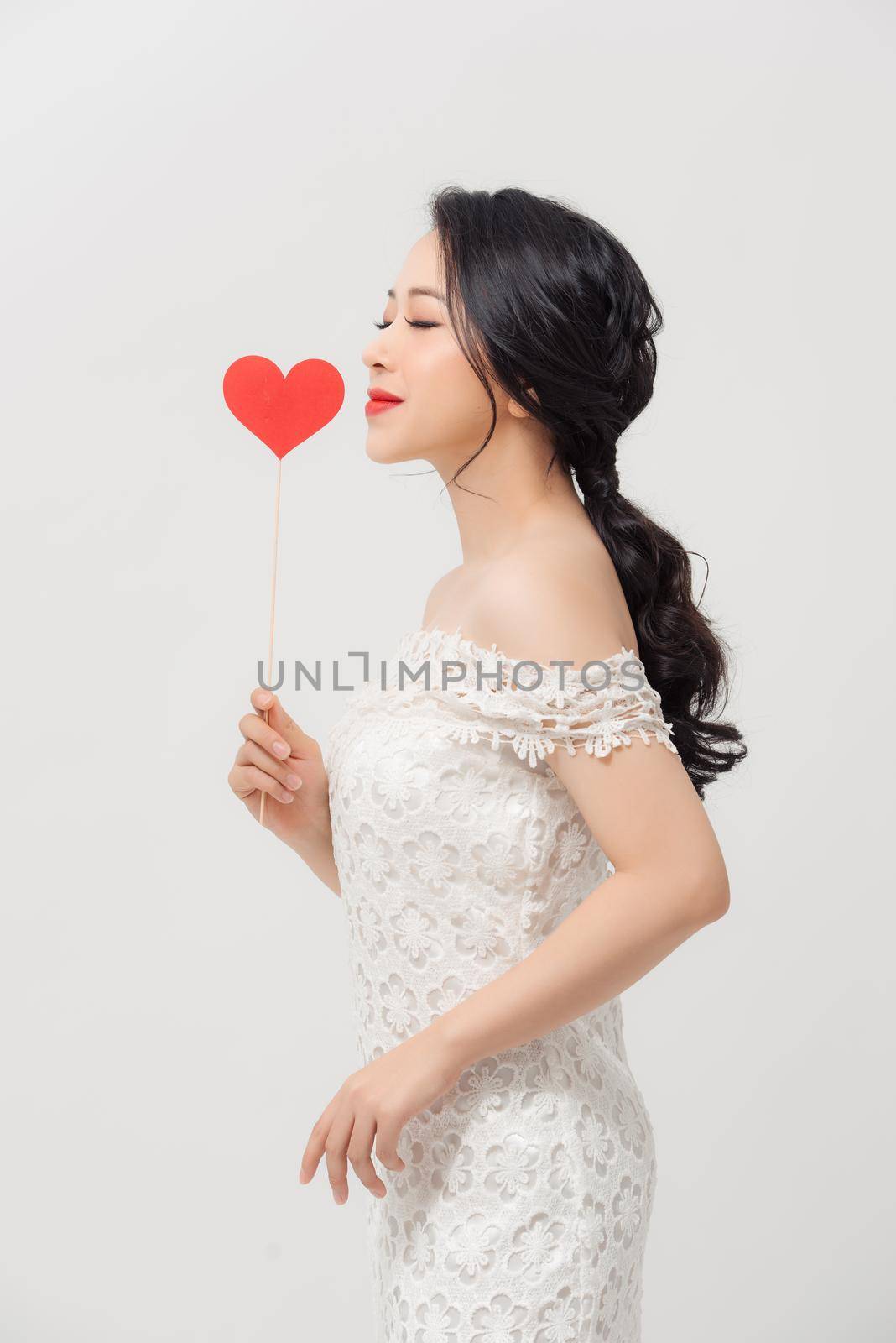 Attractive young Asian woman holding love sign when standing over white background. by makidotvn