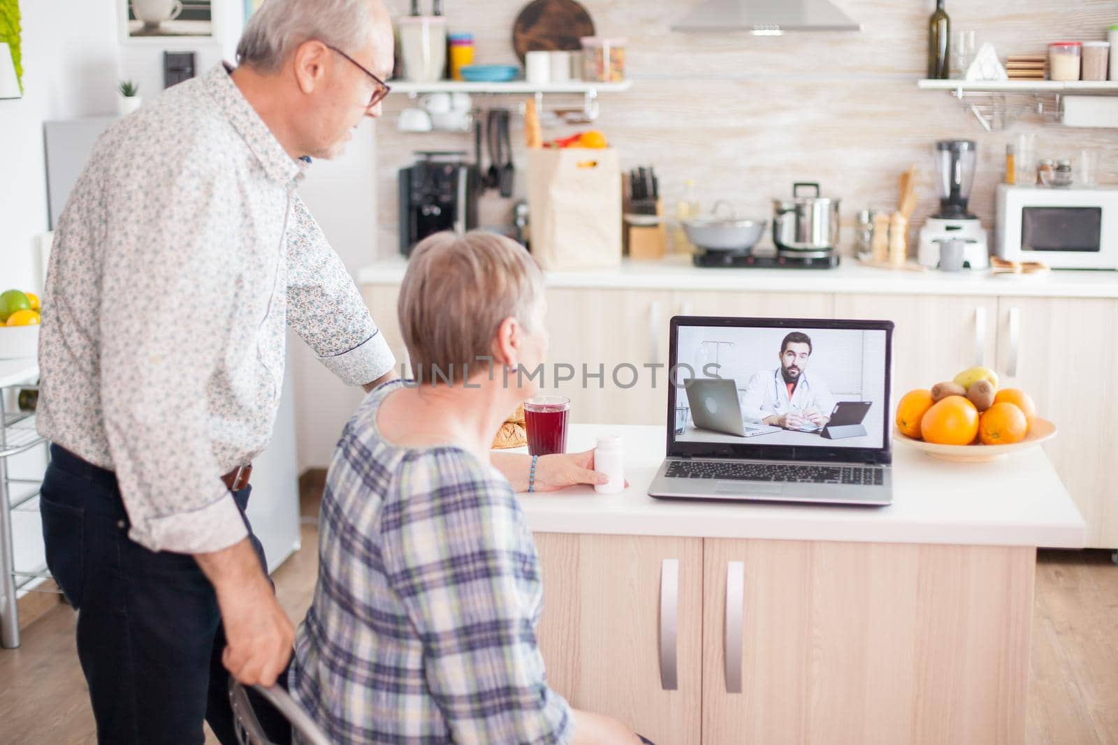 Doctor on telemedicine for senior couple. Video conference with doctor using laptop in kitchen. Online health consultation for elderly people drugs ilness advice on symptoms, physician telemedicine webcam. Medical care internet chat.