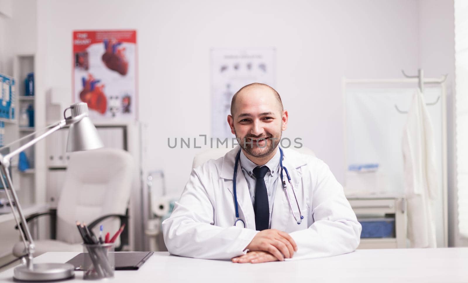 Portrait of successful young doctor in hospital office wearing white coat smiling at camera.