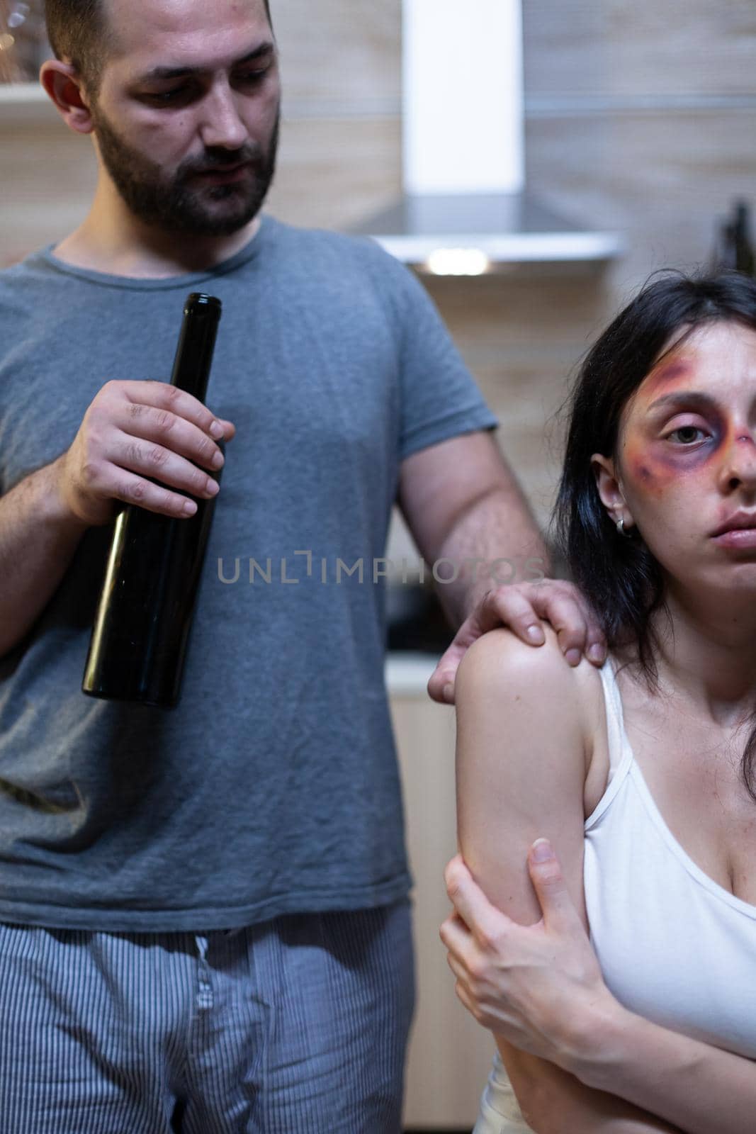 Alcoholic husband harassing abused wife with bruises. Violent man holding bottle of alcohol threatening terrified woman. Victim of domestic violence and physical trauma, marriage problem.