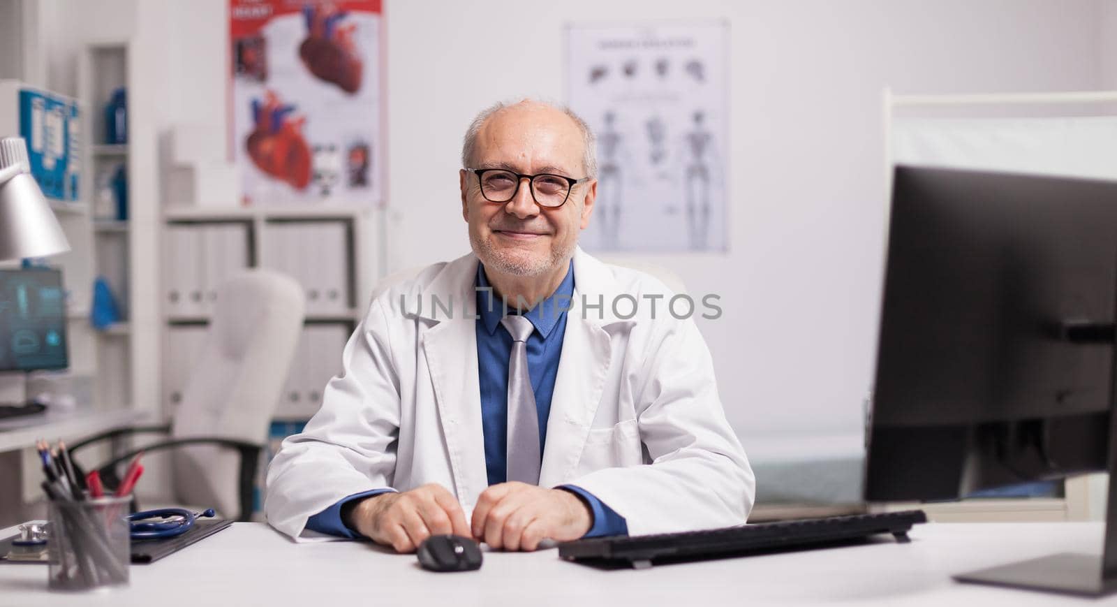 Portrait of senior doctor smiling in hospital cabinet looking at the camera.