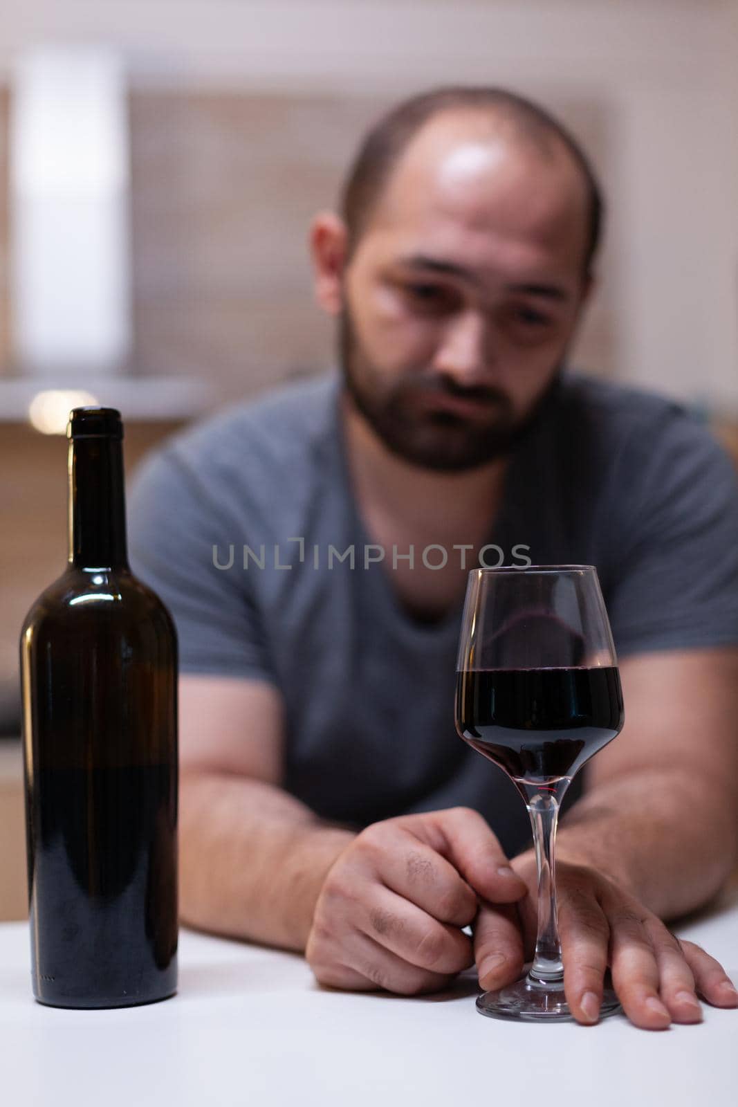 Close up of bottle and glass of wine prepared for man feeling unhappy and lonely. Person drinking alcoholic beverage, booze, liquor while being alone in kitchen. Intoxicated adult