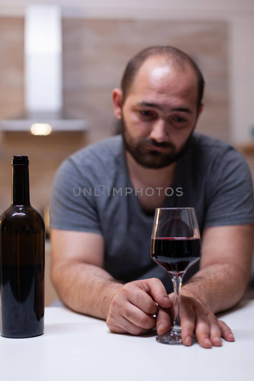 Close up of glass with wine for lonely man in kitchen by DCStudio