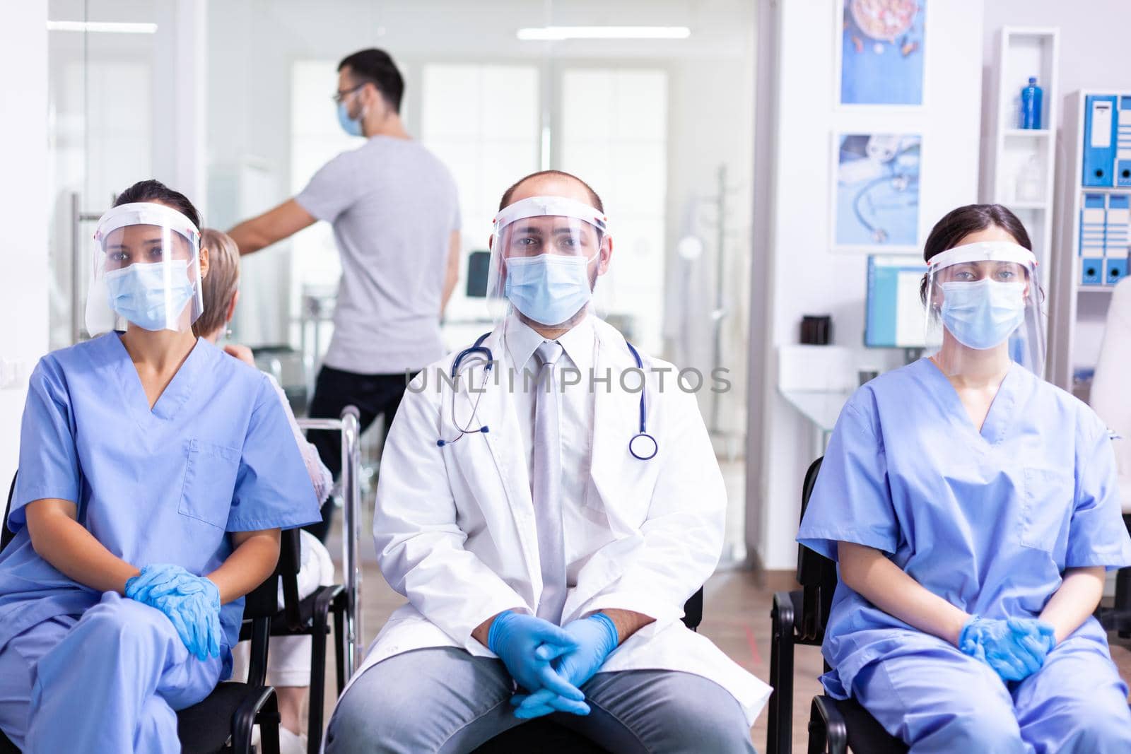 Group of medical personnel in hospital waiting area with visor and face mask against covid-19 to prevent infection. Wearing white coat and stethoscope.