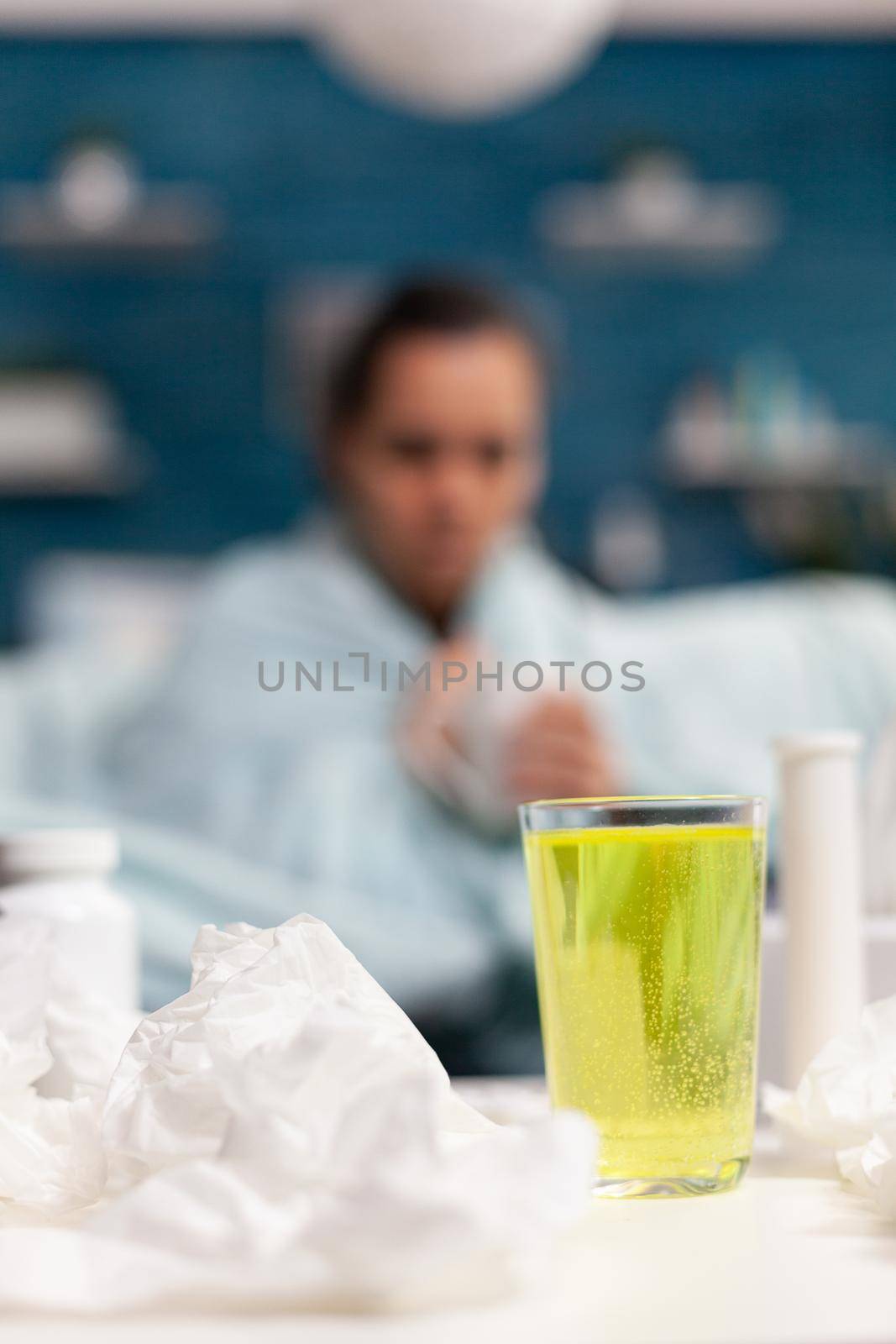 Cold young woman sitting at home on sofa with mug of tea against sickness disease illness. Caucasian person with temperature virus symptoms drinking warm vitamins from mug