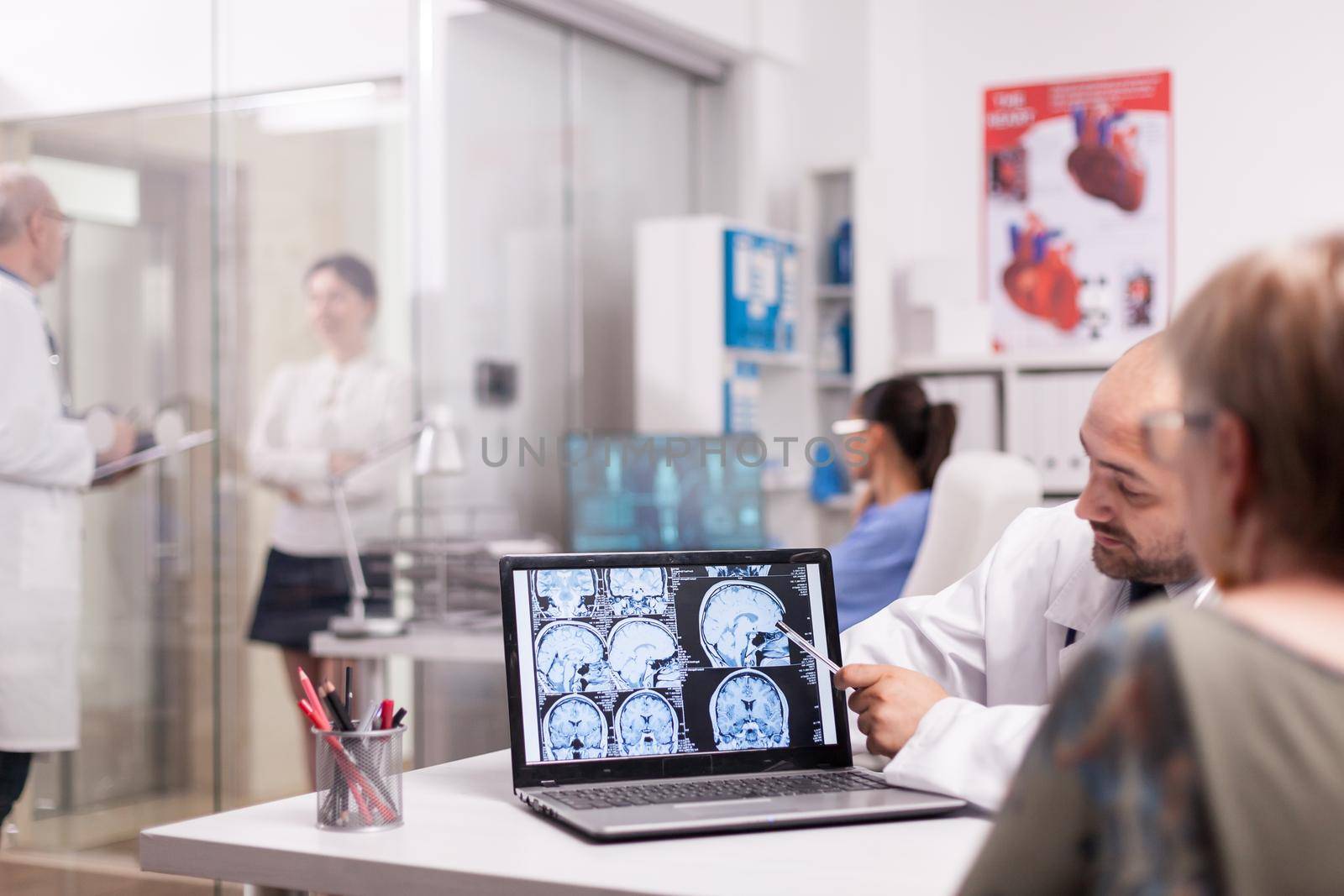 Radiologist pointing at brain ct scan on laptop screen during senior woman check up in hospital office. Mature doctor in white coat discussing with sick young woman in clinic corridor.