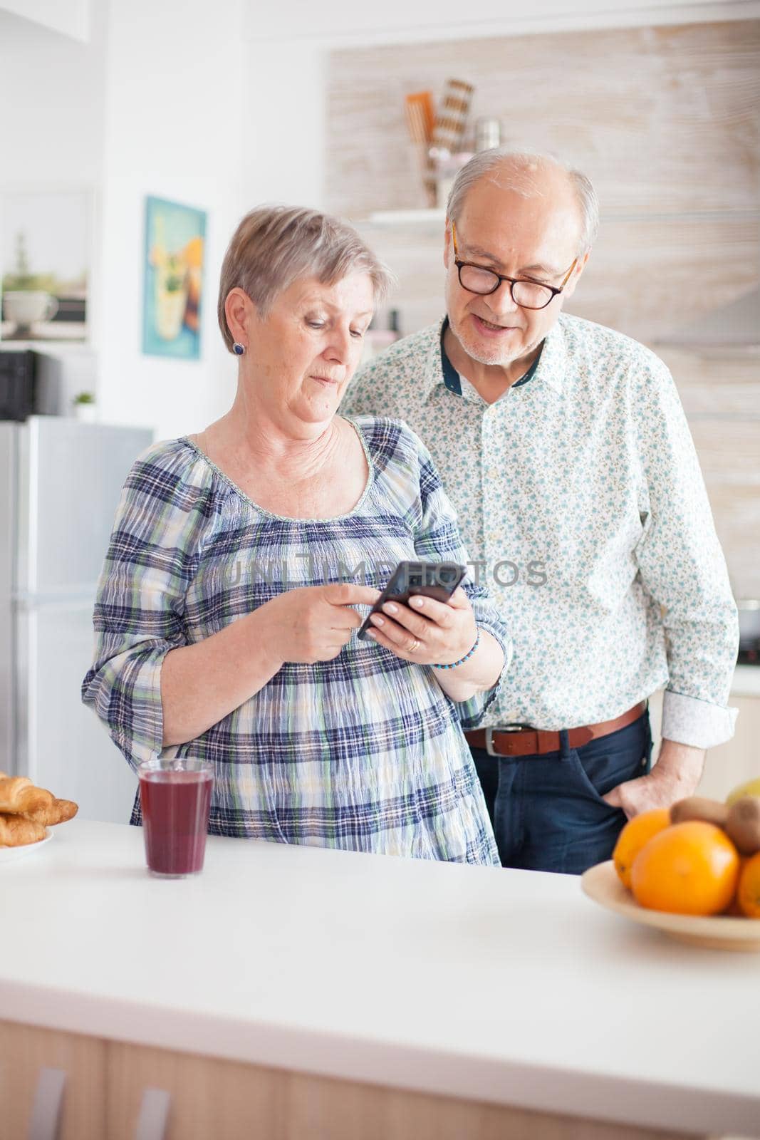 Retired couple browsing on smartphone in their cozy and bright kitchen.