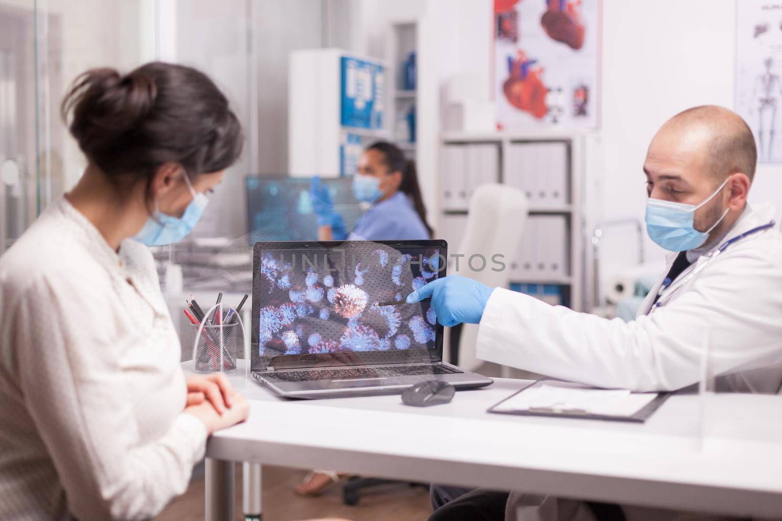 Doctor with protection mask pointing at coronavirus animation during patient consultation.