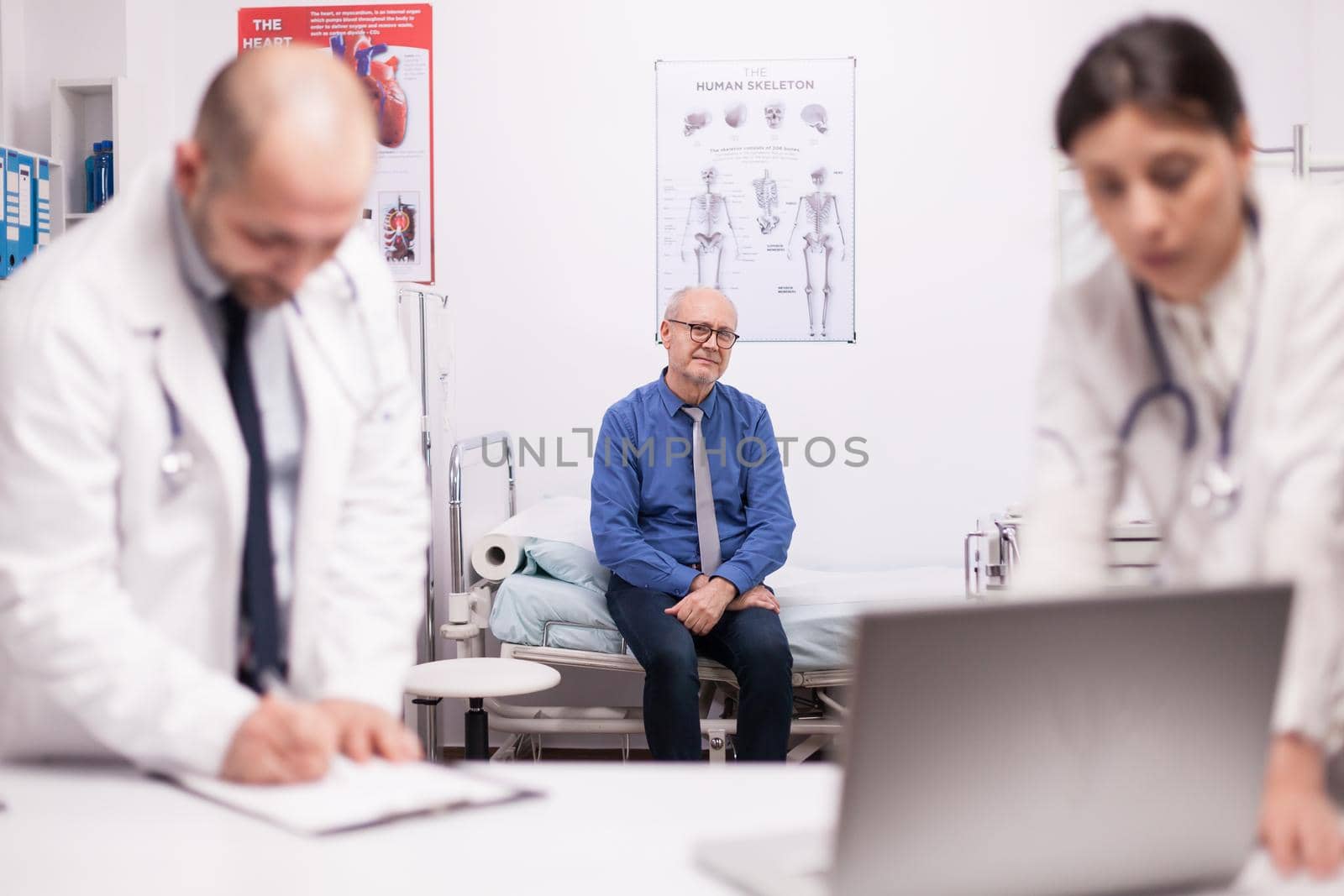 Scared elderly patient waiting for diagnosis from team of doctors in hospital office after examination. Old man during medical check up. Medics in white coat.