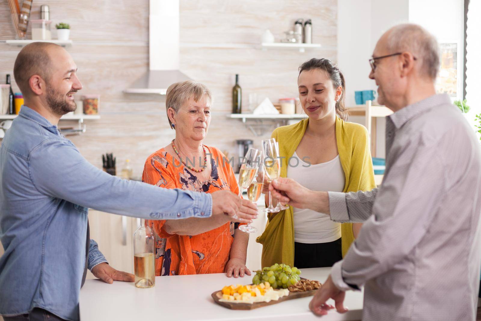 Family clinking wine glasses in kitchen during lunch. Celebrating toasting together happy extended family