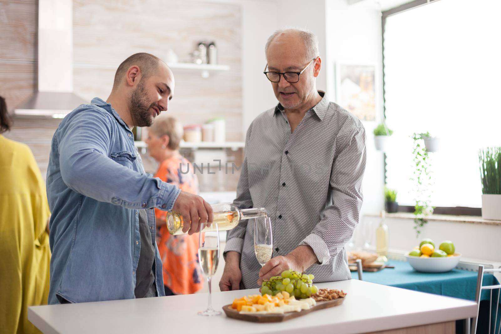 Man pouring wine to his father in kitchen during family lunch.
