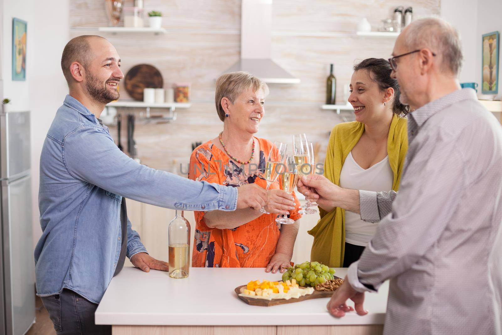 Multigeneration family clinking glasses with wine in home kitchen during reunion.