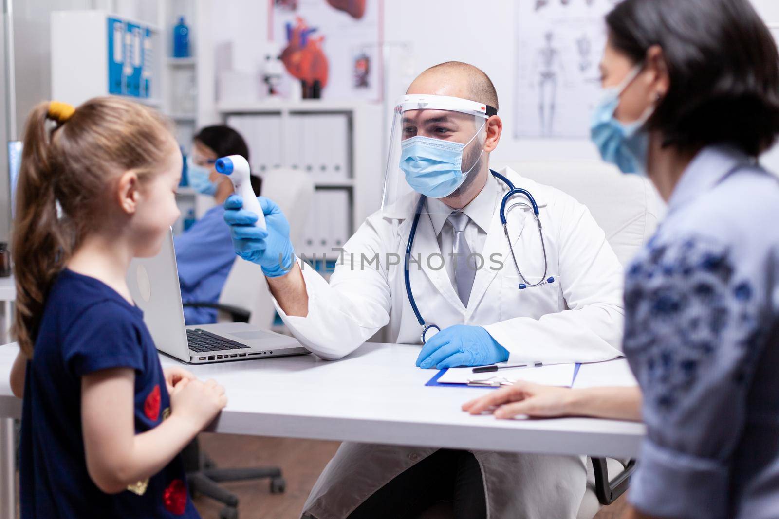 Pediatrician wearing face mask agasint coronavirus taking body temperature of child in hospital office. Health doctor specialist providing health care services consultations.