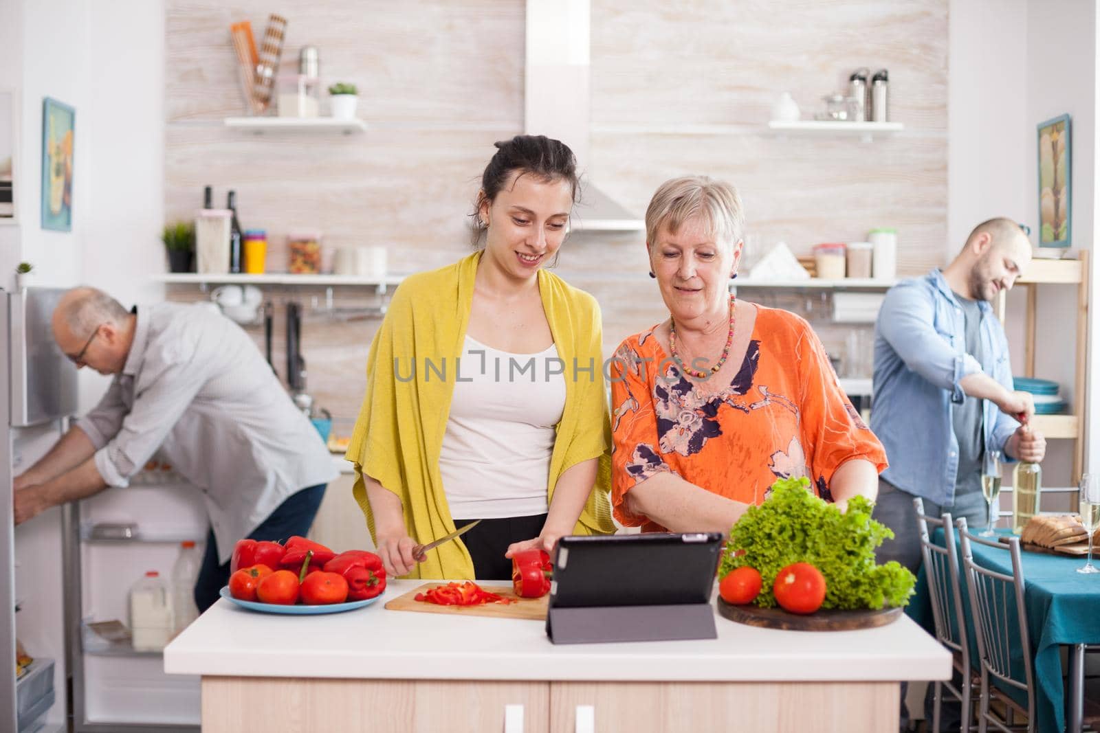 Senior woman watching salad recipe on table while cooking together with her daughter in kitchen. Mother daughter preparing lunch.