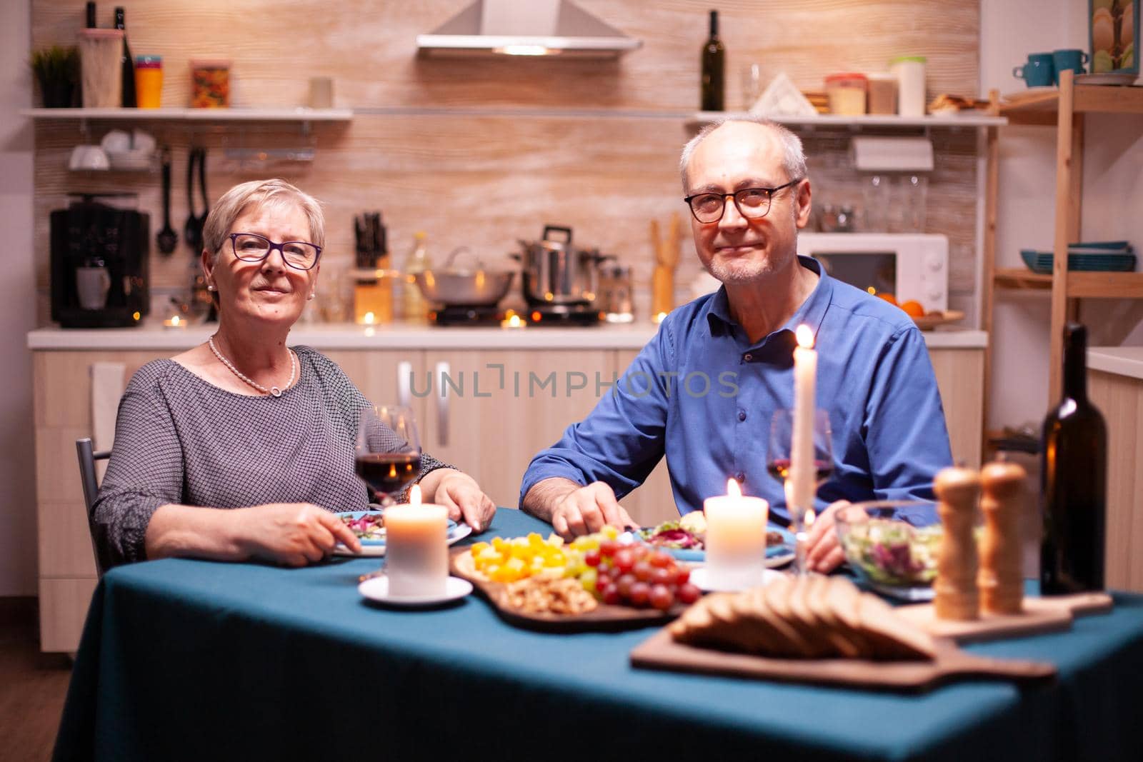 Senior couple looking at camera during relationship celebration with festive dinner in kitchen. Aniversary, leisure, retired, family, romantic