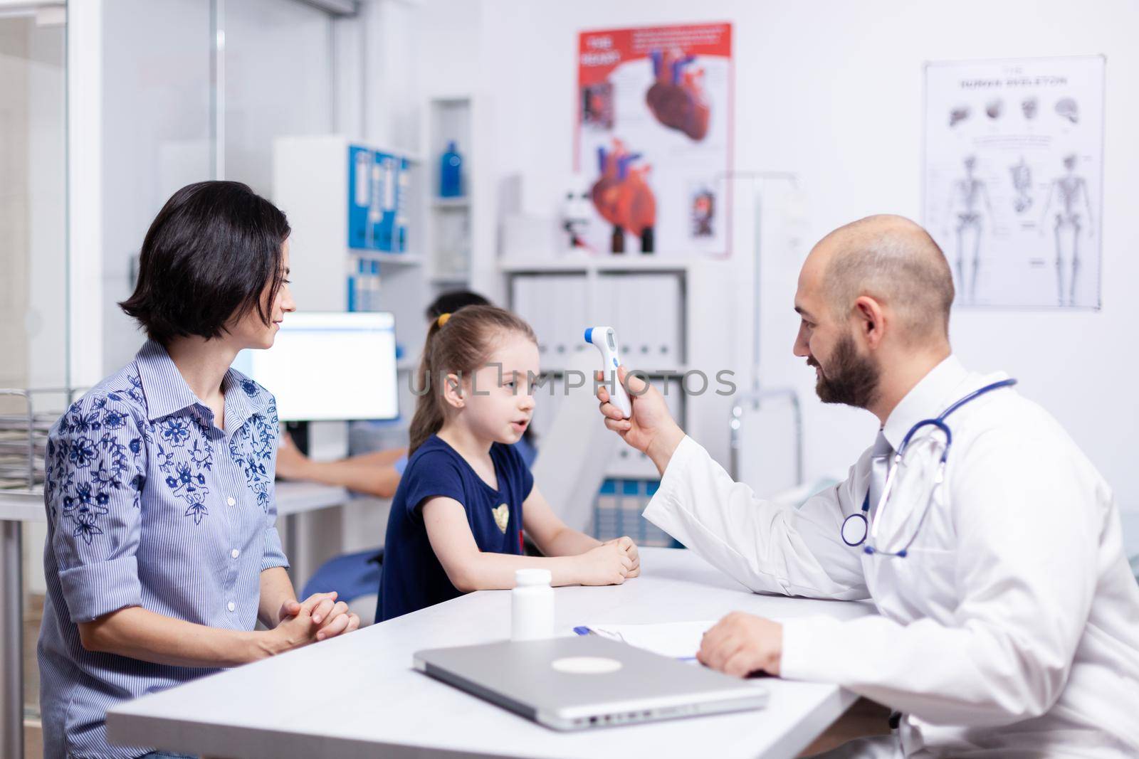 Pediatrician checking child temperature using digital thermometer in medical office. Healthcare physician specialist in medicine providing health care services treatment examination.