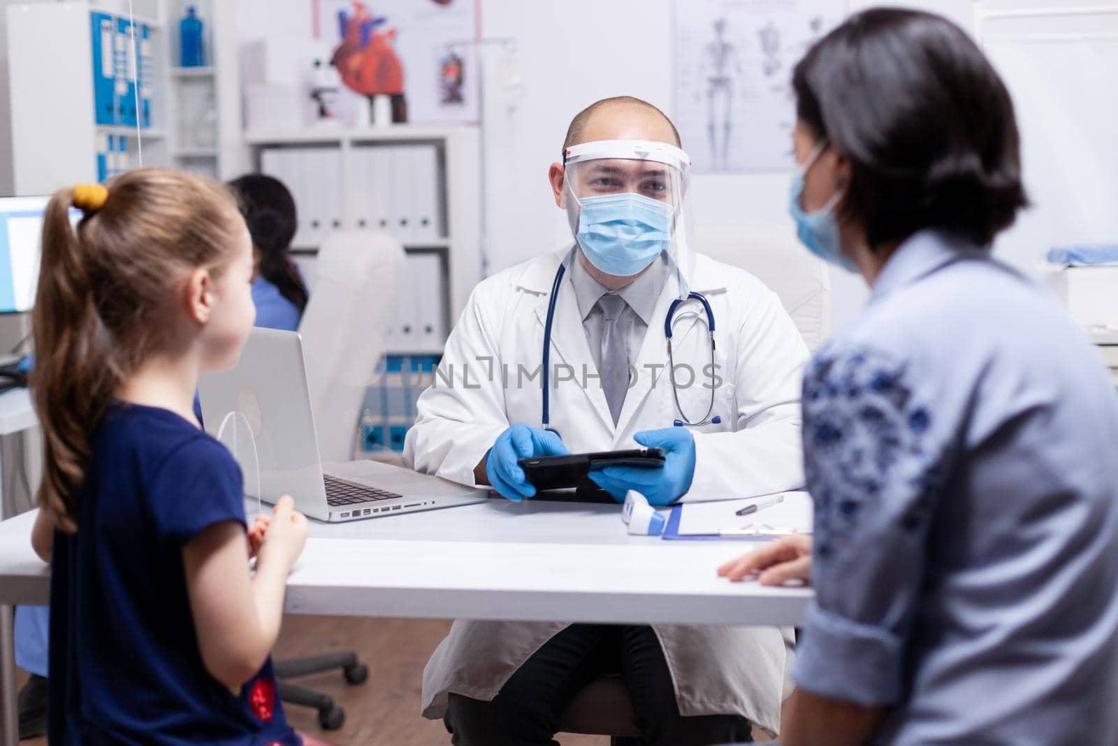 Doctor talking about child treatment with mother during coronavirus pandemic wearing face mask and holding tablet pc. Pediatrician specialist with protection mask providing health care.