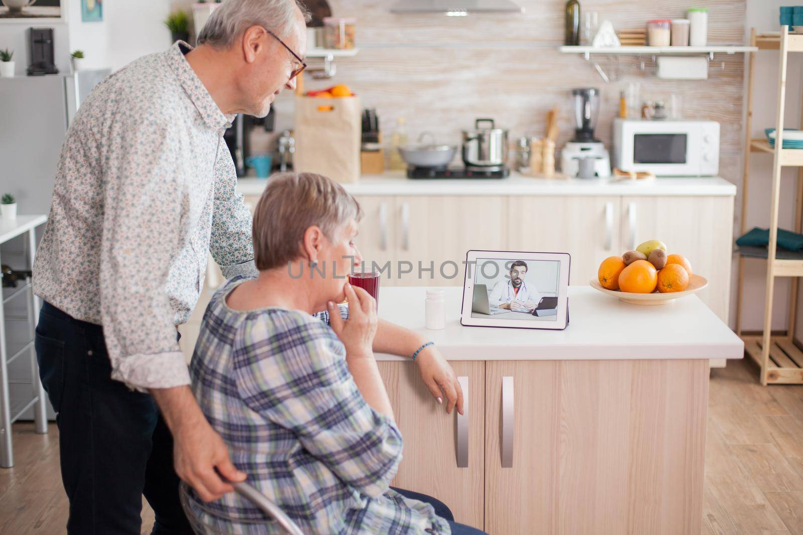 Worried senior woman in medical check with her husband next. Video conference with doctor using laptop in kitchen. Online health consultation for elderly people drugs ilness advice on symptoms, physician telemedicine webcam. Medical care internet chat