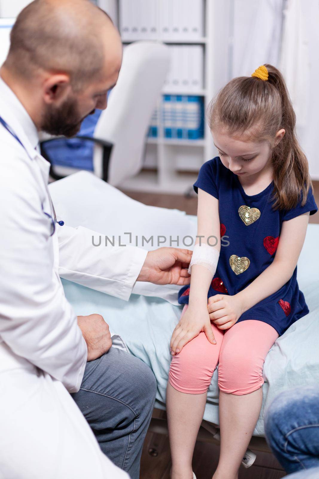 Pediatrician bandaging child by DCStudio