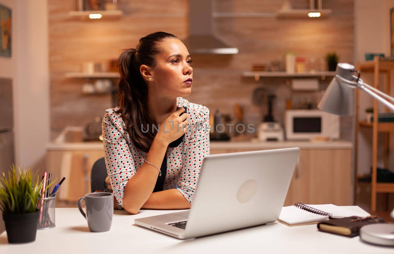 Woman thinking about her career while working on a deadline late at night in home kitchen. Employee using modern technology at midnight doing overtime for job, business, busy, career, network, lifestyle ,wireless.