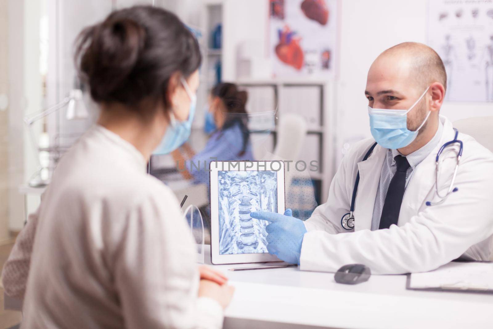 Doctor with mask against covid 19 pointing at radiography on tablet pc during patient examination.
