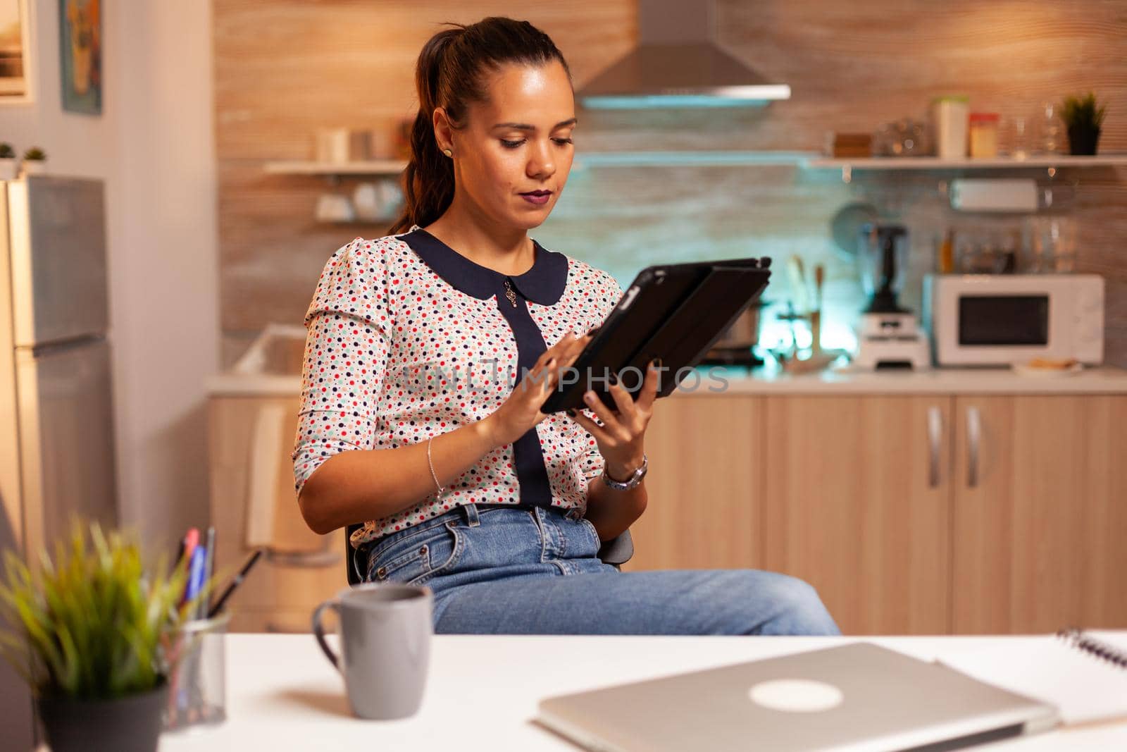 Businesswoman using tablet pc while working from home kitchen. Employee using modern technology at midnight doing overtime for job, business, busy, career, network, lifestyle ,wireless.