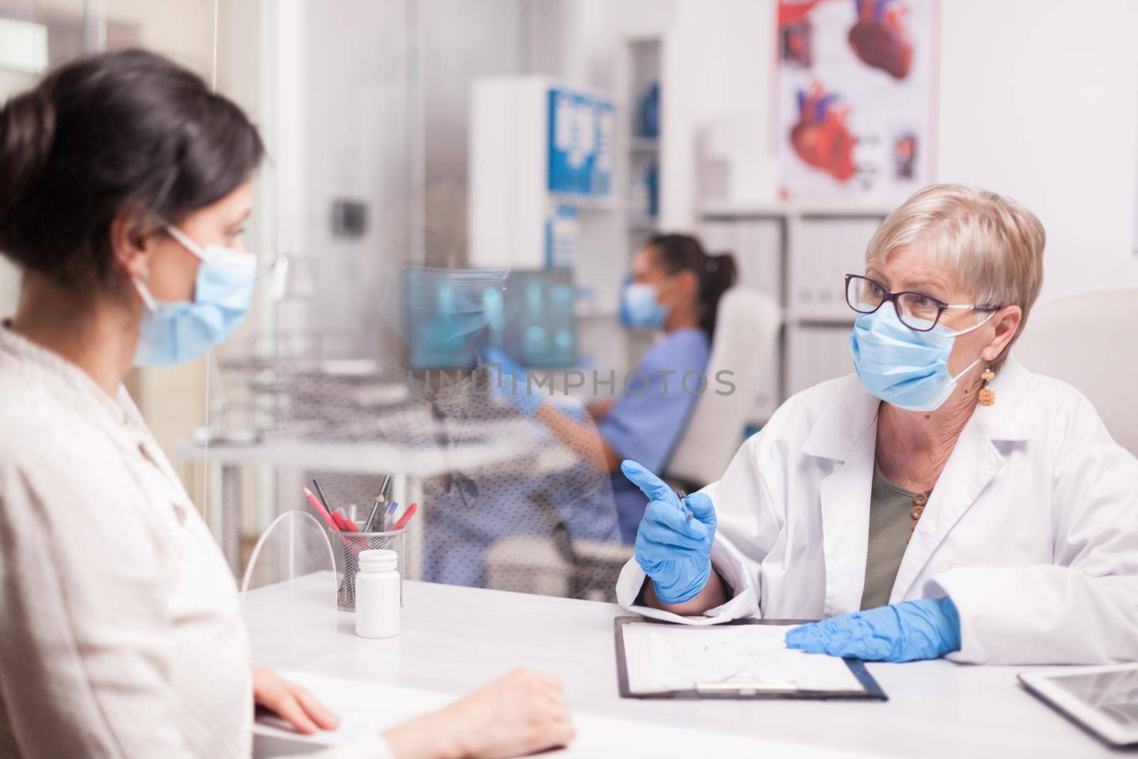 Senior doctor with face mask against coronavirus during consultation with female patient. Nurse wearing blue uniform.