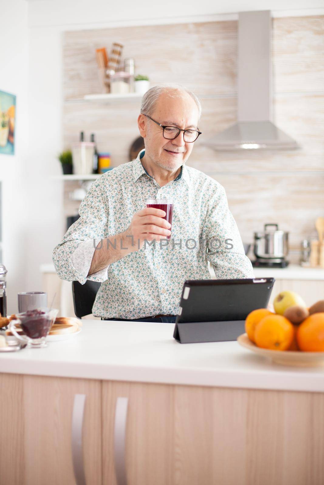 Elderly man surfing on internet using tablet computer during breakfast in kitchen. Senior person with tablet portable pad PC in retirement age using mobile apps, modern internet online information technology with touchscreen