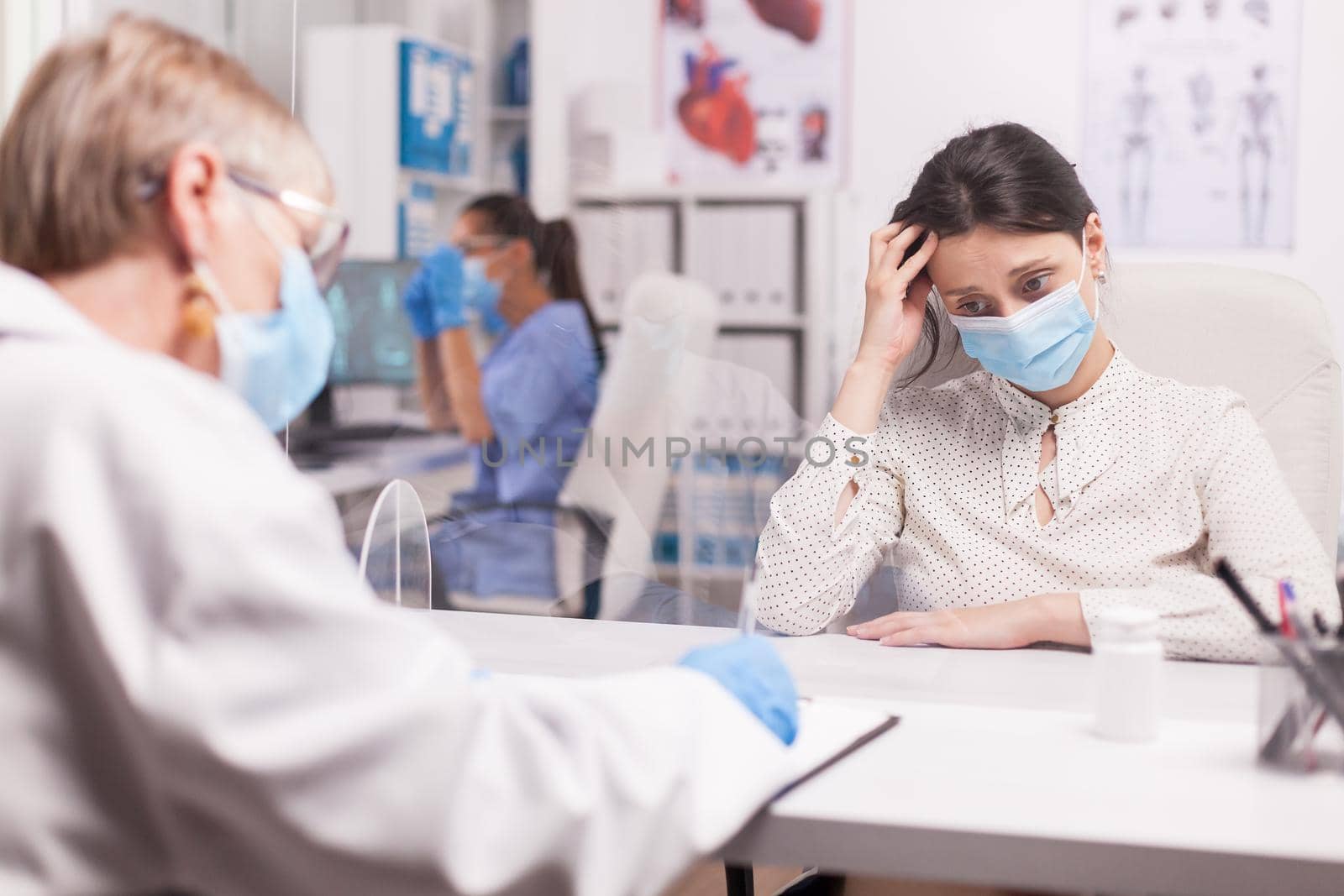 Young woman with protection mask against covid-19 crying during examination with doctor in hospital room.